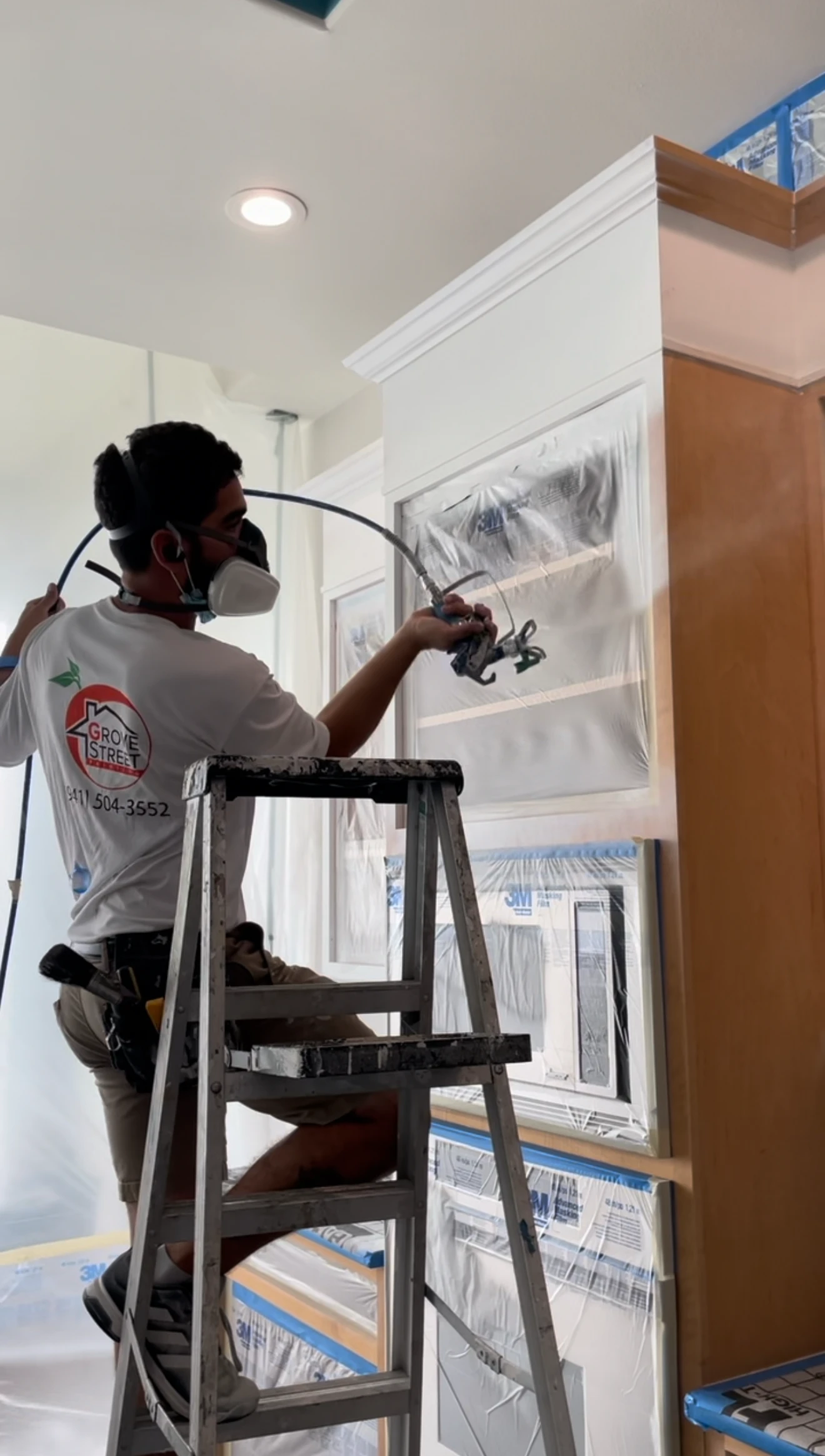 Sarasota cabinet painter spraying door fronts from a ladder for even coverage