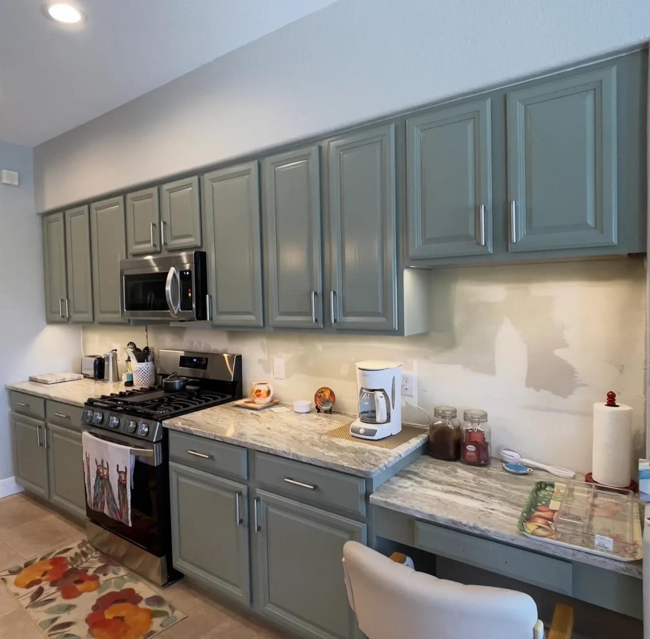 Long run of sage green painted kitchen cabinets with silver bar pulls