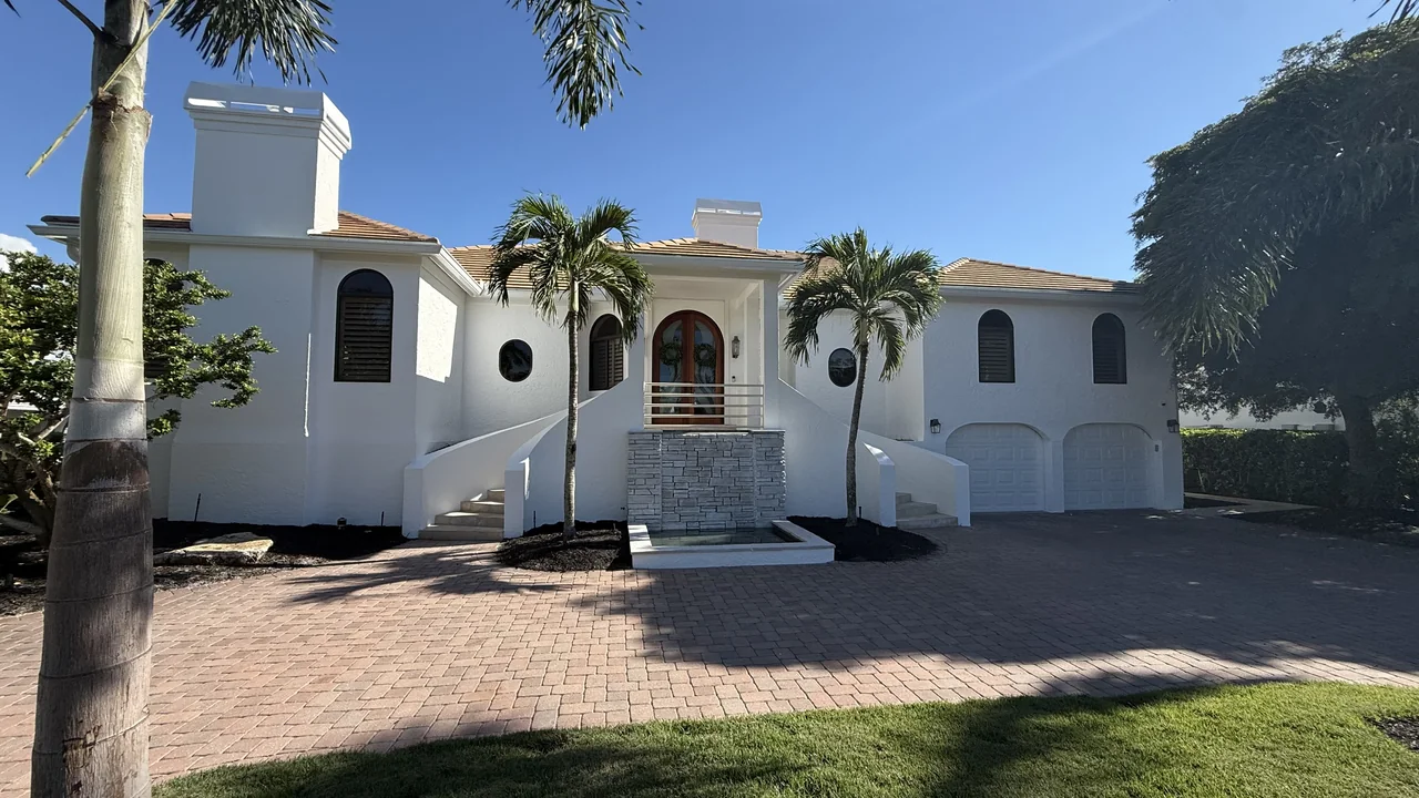 Finished white stucco home with arched windows, palms and a paver drive after an exterior repaint