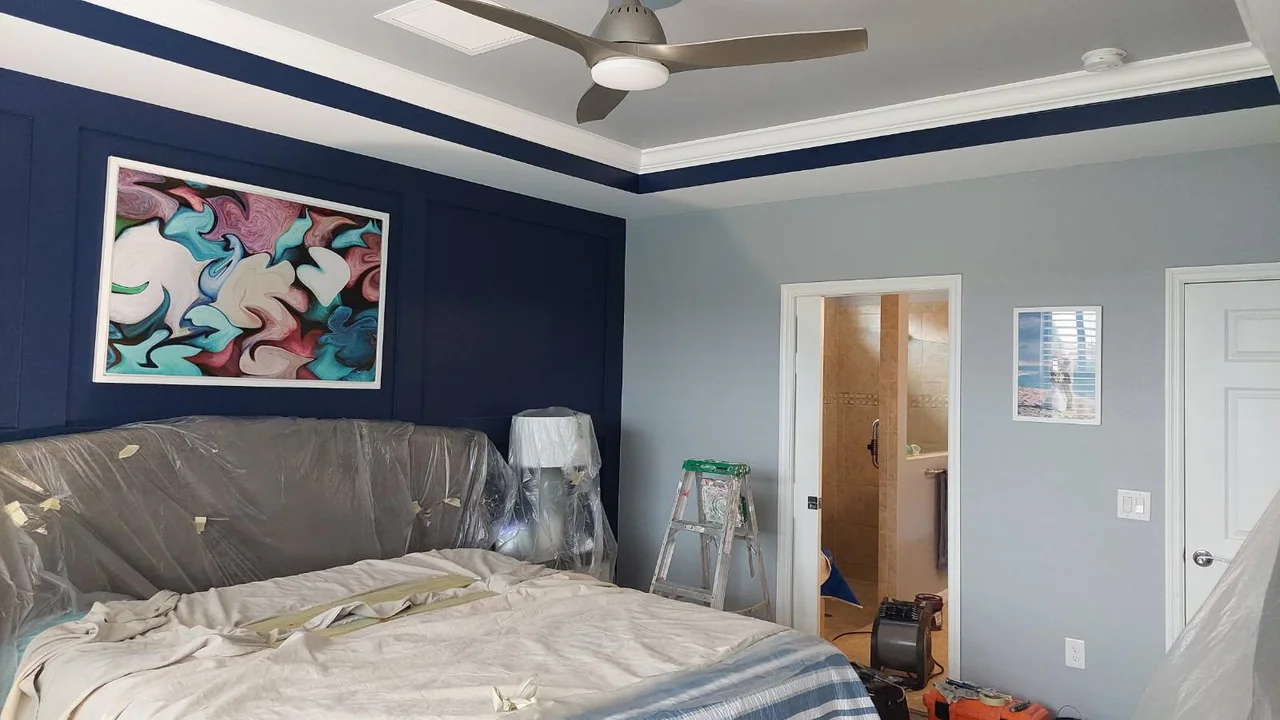 Bedroom mid-project with the bed and lamps wrapped in plastic beside a navy accent wall