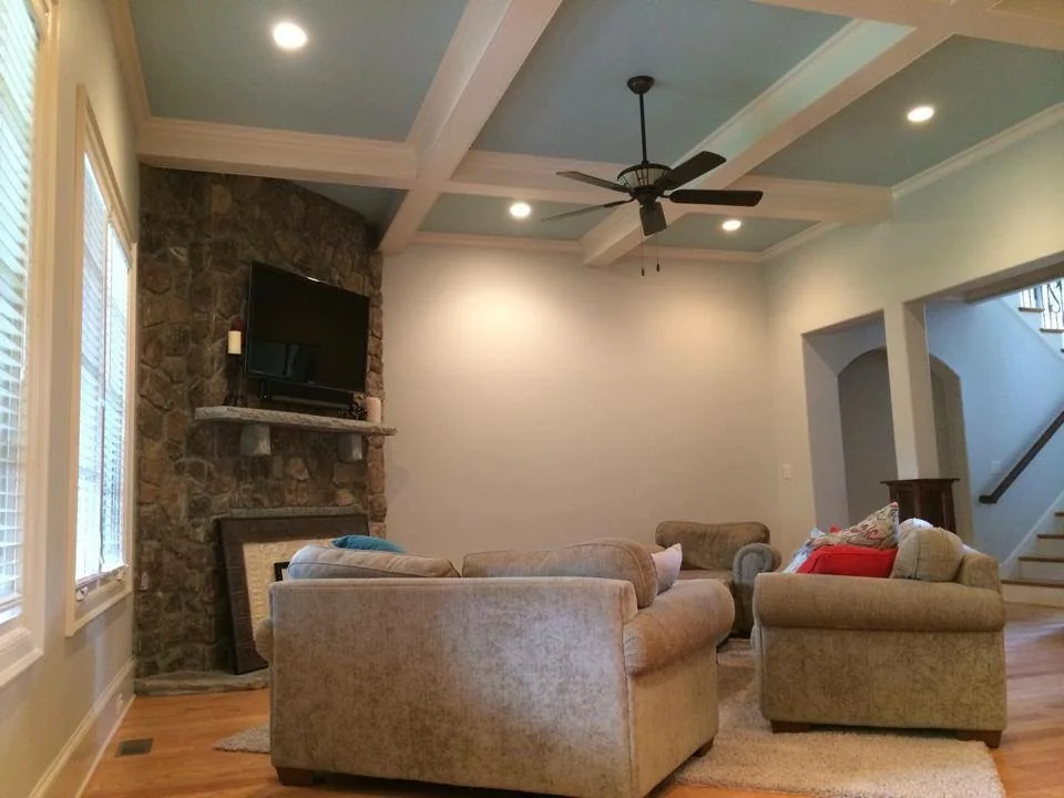 Family room with a soft blue coffered ceiling, white beams and a stone fireplace wall