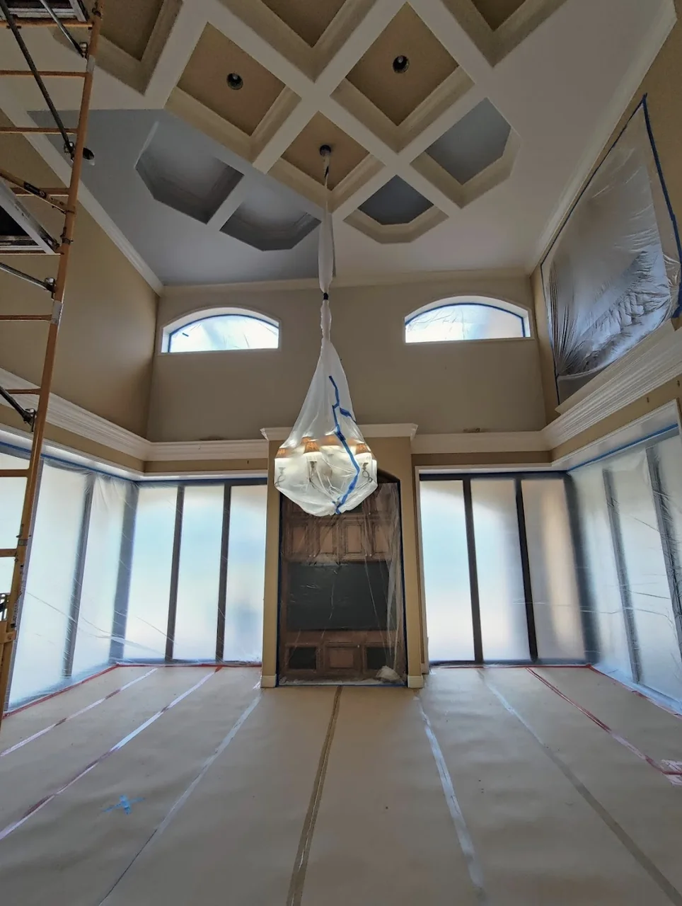 Two-story room with a coffered ceiling, windows sealed in plastic and the floor masked before spraying